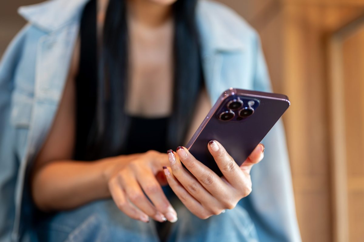 A close-up of a woman in a denim jacket sits in a coffee shop, using her smartphone.